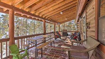 A wooden deck with benches and chairs, a table, and a view of trees.