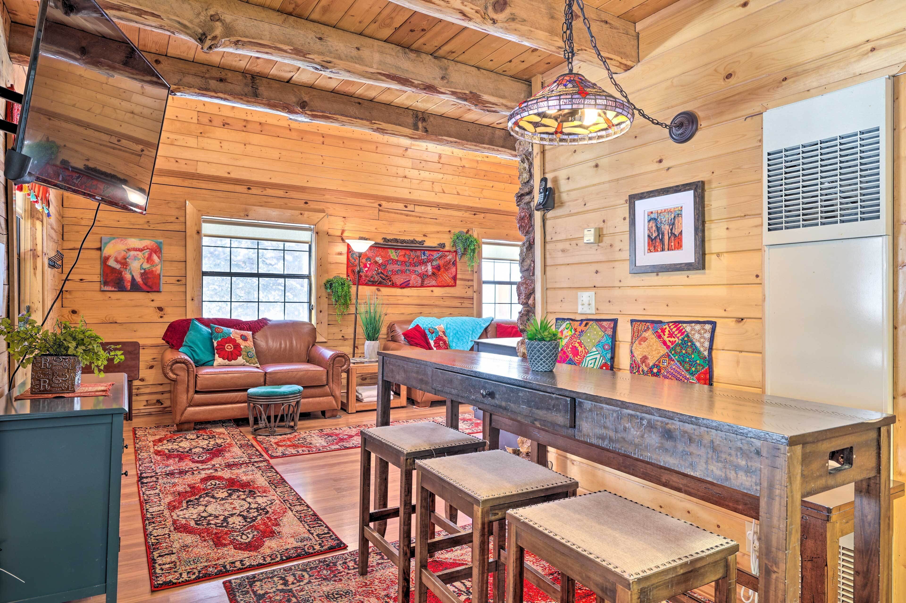 A cozy cabin interior with wooden walls, a dining area, a sofa, and a coffee table.