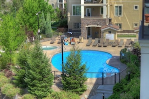Un área de piscina con sillones de descanso, una piscina pequeña y un edificio con balcones.