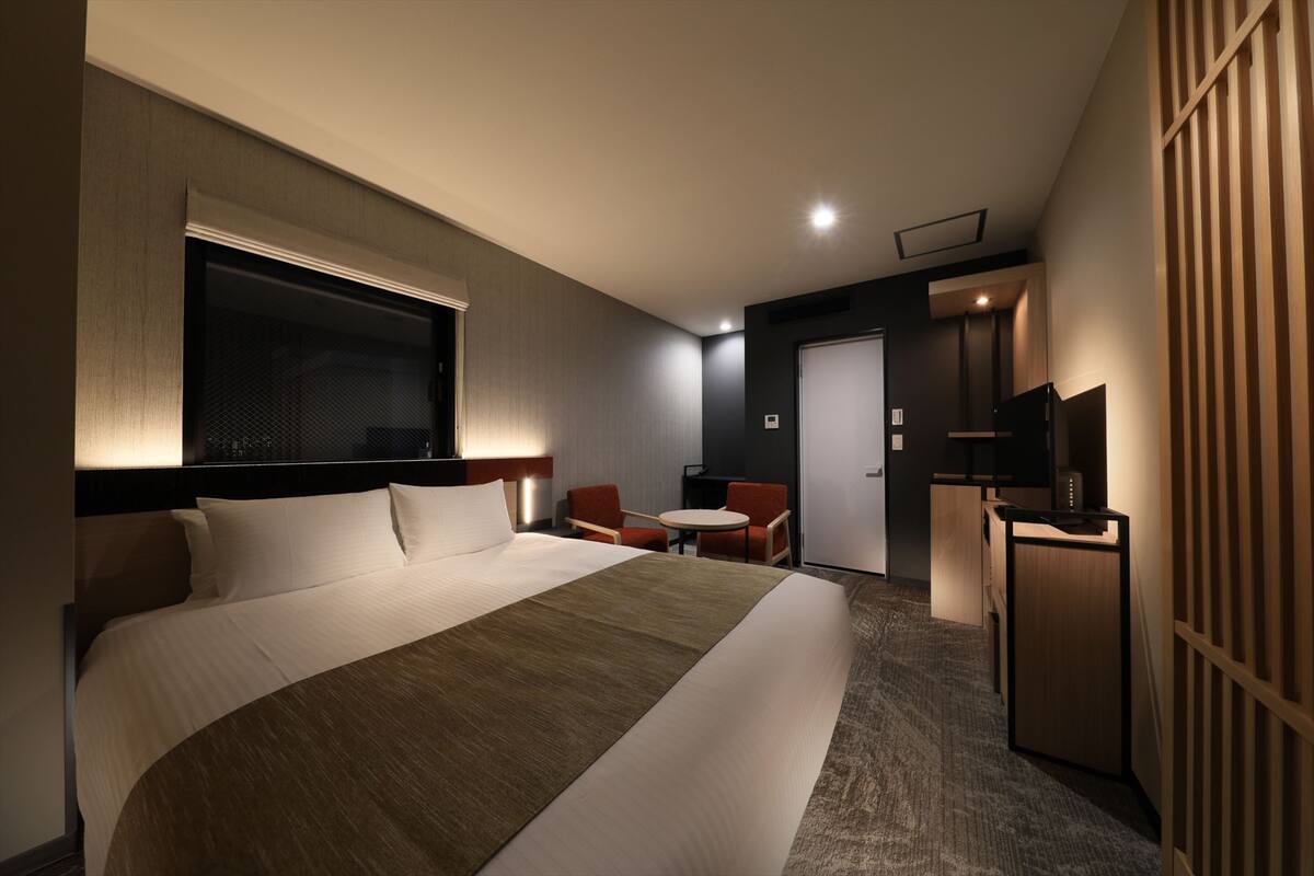 A hotel room with a large bed, a desk, a chair, and a television.