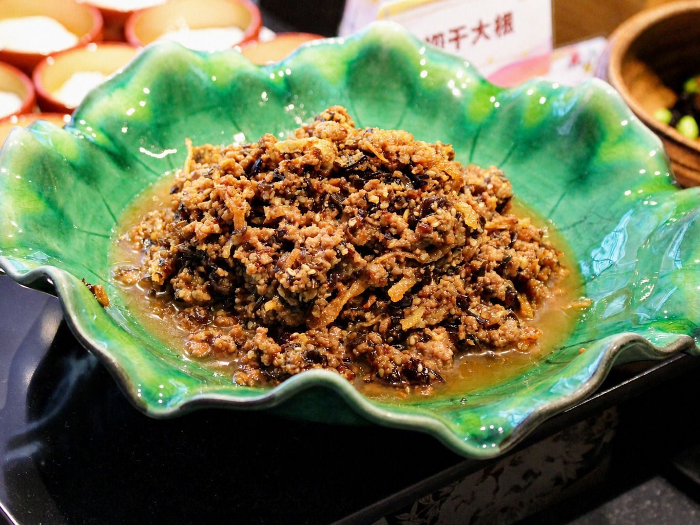 A green bowl filled with a brownish food item, possibly a dish with a sauce, placed on a black surface.
