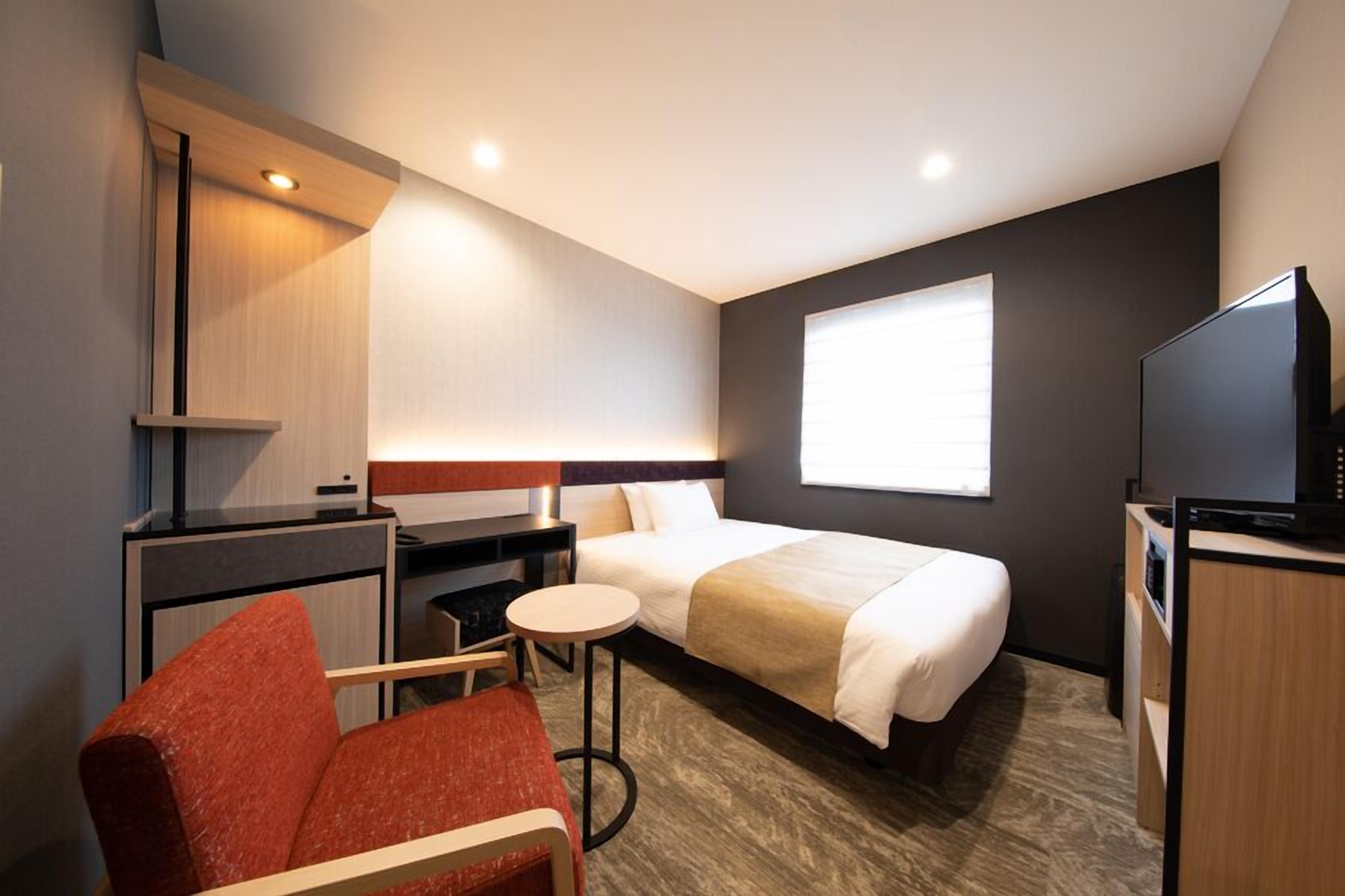 Ein Hotelzimmer mit Bett, Schreibtisch, Stuhl, Fernseher und Fenster.