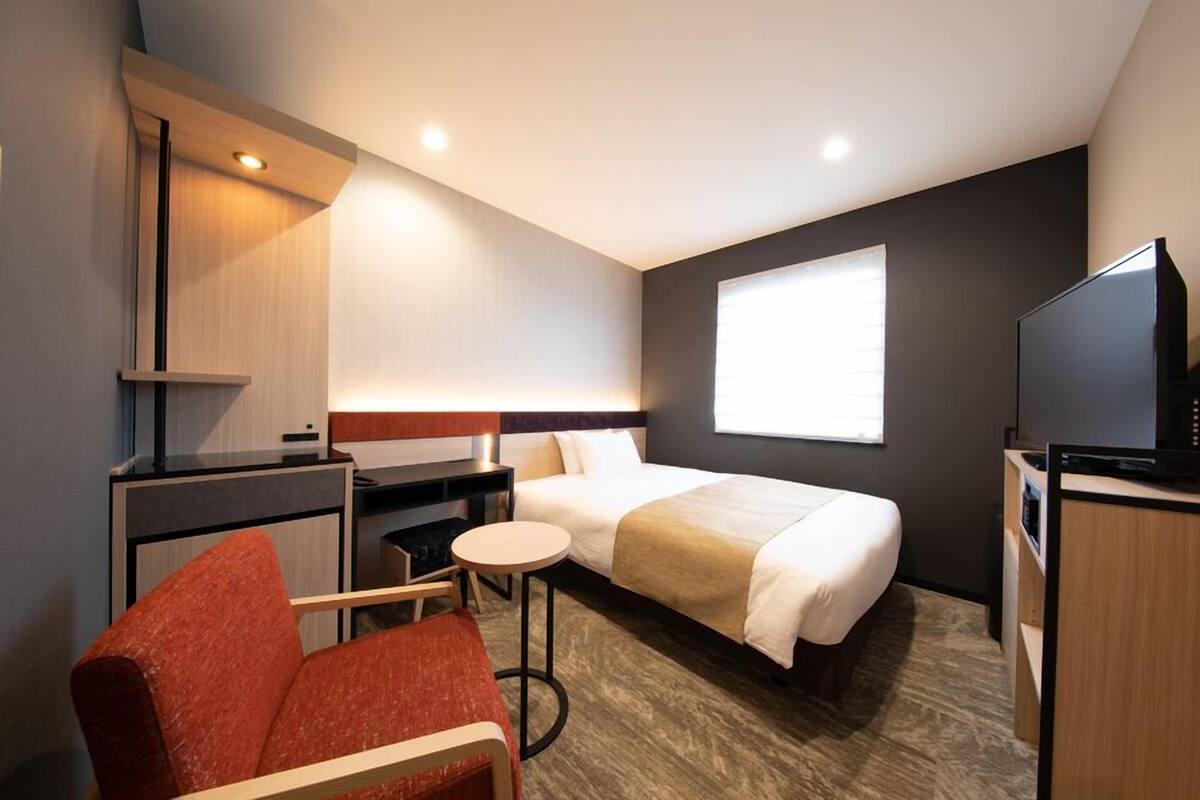 A hotel room with a bed, a desk, a chair, a television, and a window.