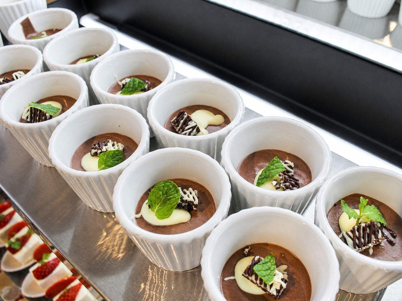 A tray of dessert cups with chocolate mousse, garnished with mint leaves and chocolate shavings.