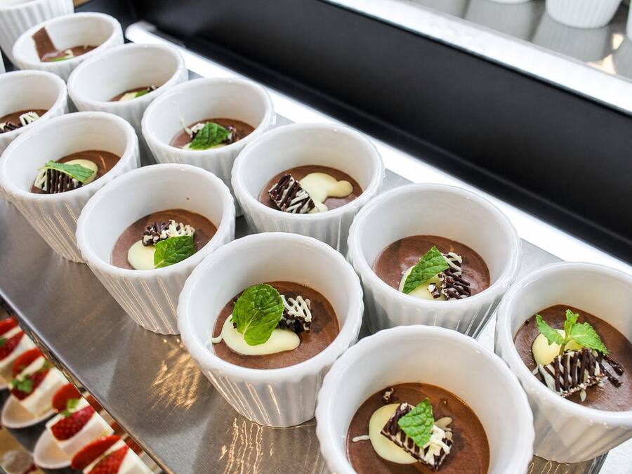 A tray of dessert cups with chocolate mousse, garnished with mint leaves and chocolate shavings.