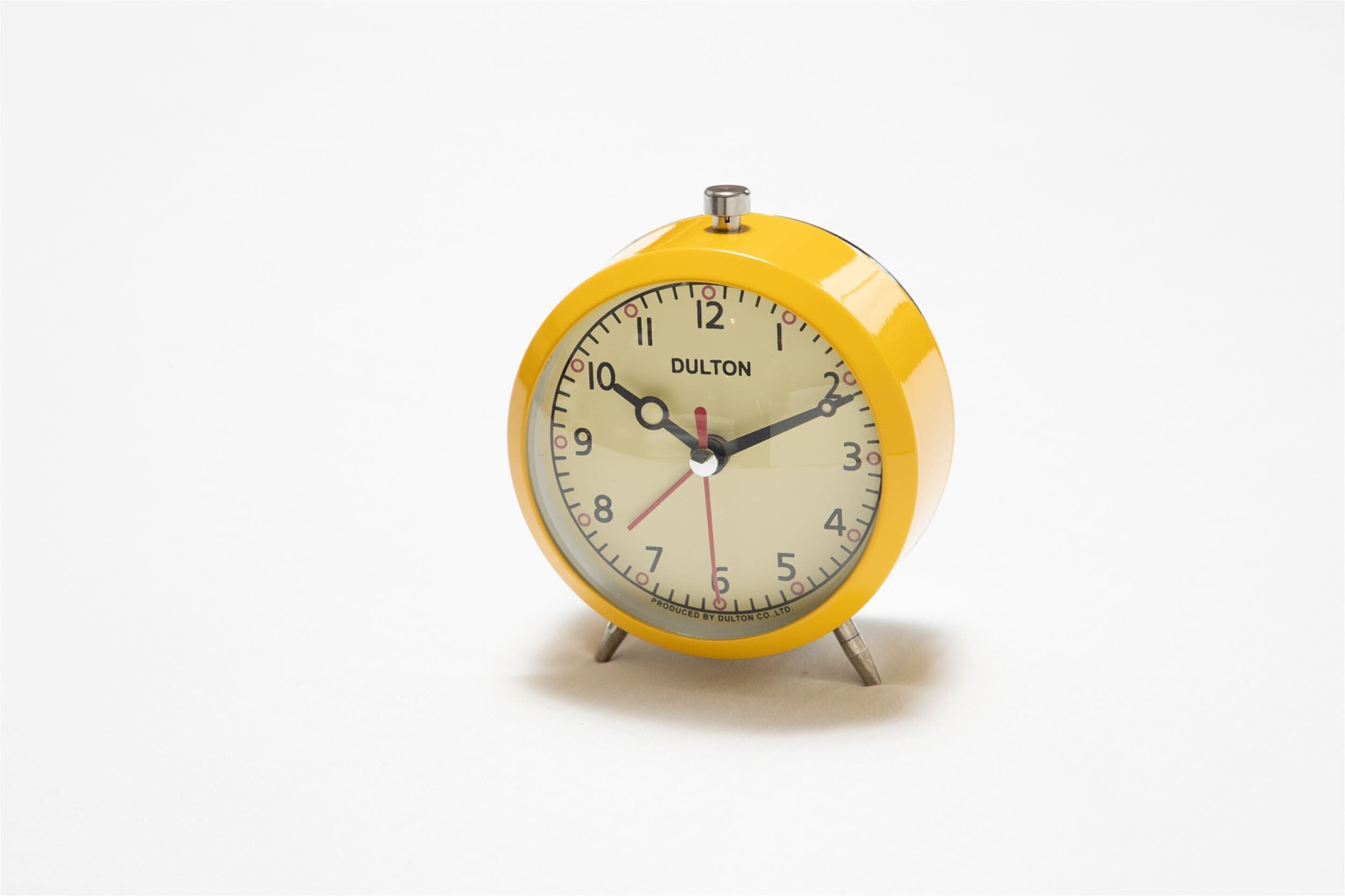 A yellow Dulton alarm clock with a white face and black numerals.