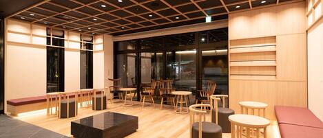 A modern interior with wooden flooring, a seating area with benches and tables, and a large window providing a view of the city.