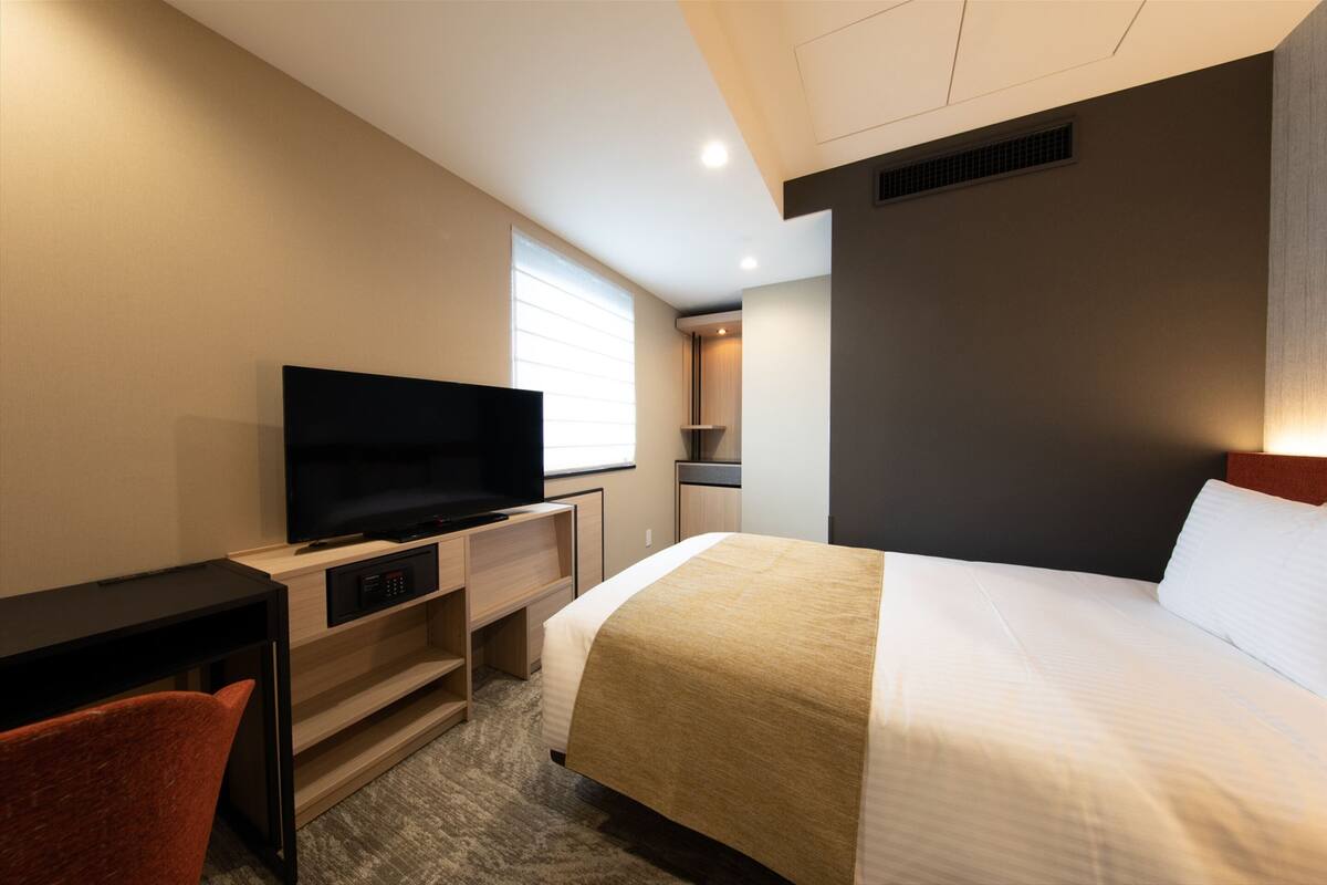 A hotel room with a bed, a TV, a desk, and a chair.