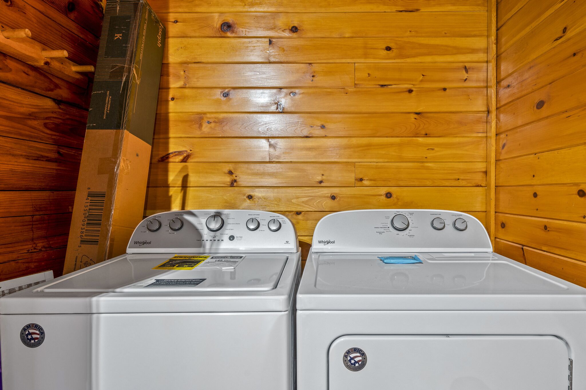 Two white Whirlpool washers in a wooden cabin with a wooden wall and a wooden floor.