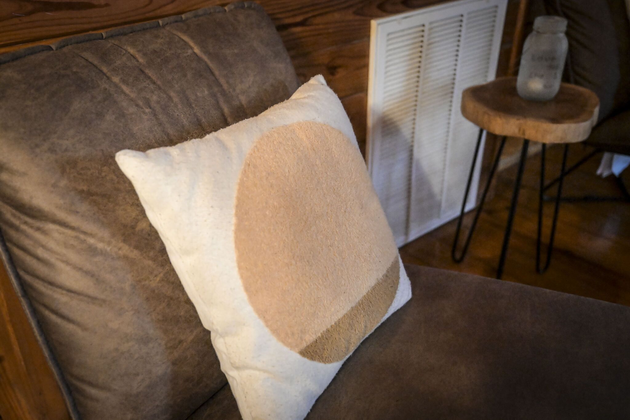 A brown sofa with a white pillow featuring a beige patch.
