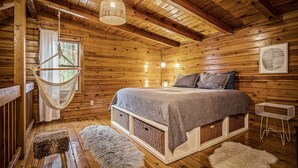 A wooden cabin bedroom with a bed, hanging light fixture, and a window with curtains. - Log Cabin w/Hot Tub & All the Amenities. Close to the Park & Pigeon Forge (sevierville)