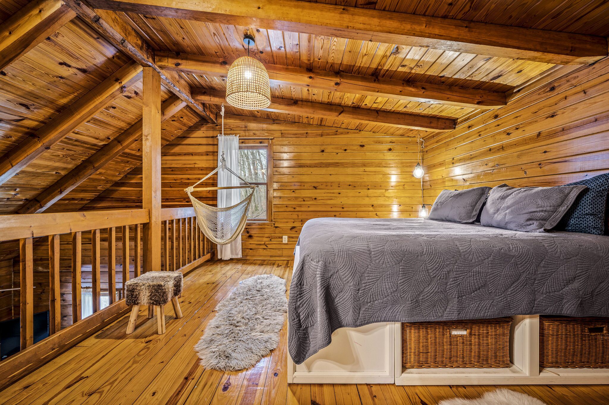 Une chambre confortable dans un chalet en bois, avec un lit, un fauteuil suspendu et une grande fenêtre.