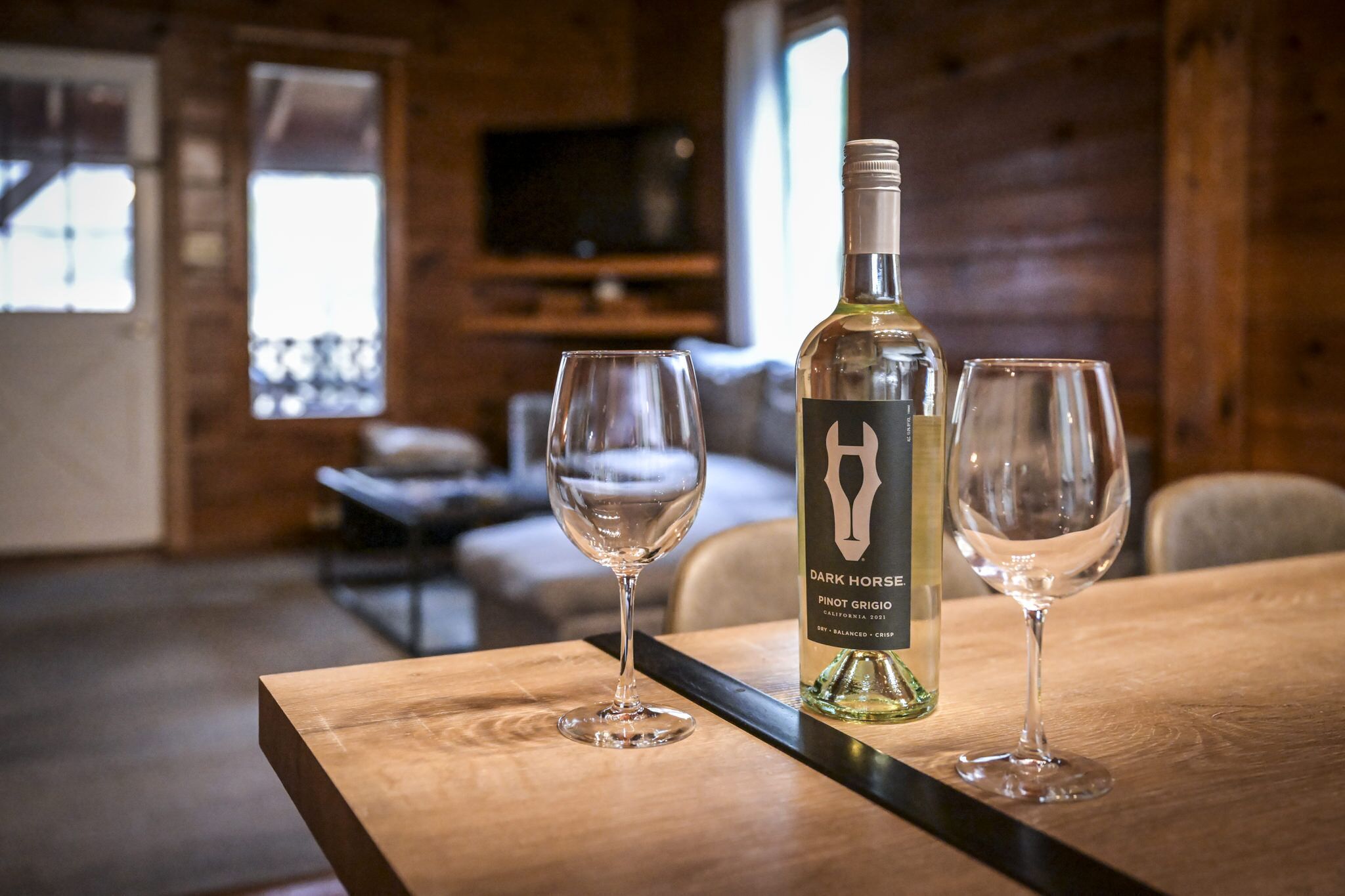 A bottle of Dark Horse Pinot Grigio on a wooden table with two empty wine glasses.