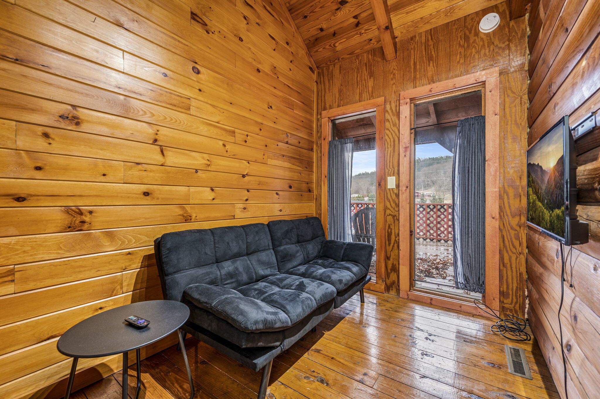 A wooden cabin interior with a black sofa, a small table, and a door leading outside.