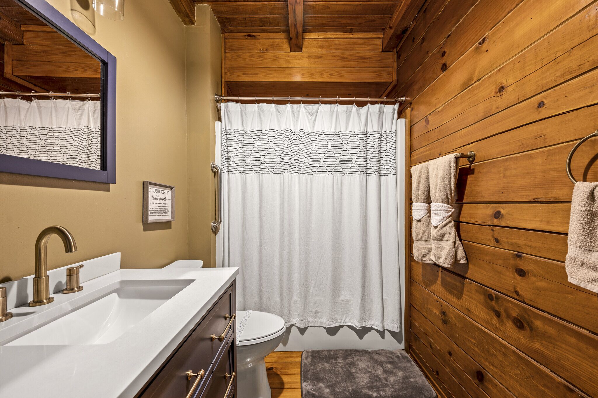 A bathroom with a wooden wall, a white sink, a toilet, and a shower curtain.