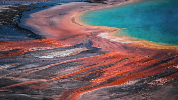 Vue aérienne d’une zone géothermique caractérisée par des dépôts minéraux distincts et une étendue d’eau turquoise.