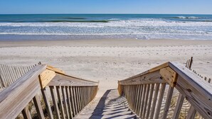 A wooden boardwalk leading to a sandy beach with ocean waves in the background.