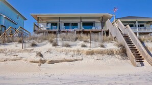 A beachfront property with a wooden staircase leading to a covered deck area, a sign reading "LIFESAVER," and a flag on a flagpole.