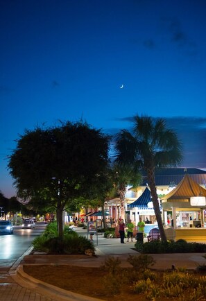A nighttime urban street scene with a crescent moon, palm trees, and illuminated buildings.