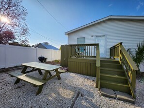 A patio area with a picnic table and a wooden deck leading to a house.