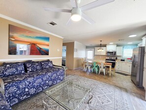 A living room with a sofa, a glass coffee table, and a painting on the wall.