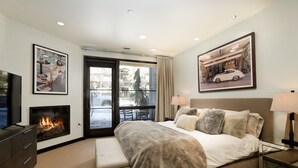 Una habitación de hotel moderna con una cama grande, una chimenea, un televisor y dos cuadros en las paredes.