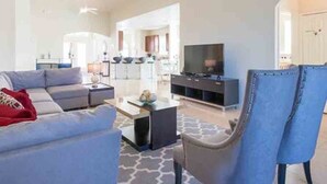 Ein modernes Wohnzimmer mit einer Couch, einem Couchtisch und einem Fernseher. Im Hintergrund befindet sich ein Essbereich.