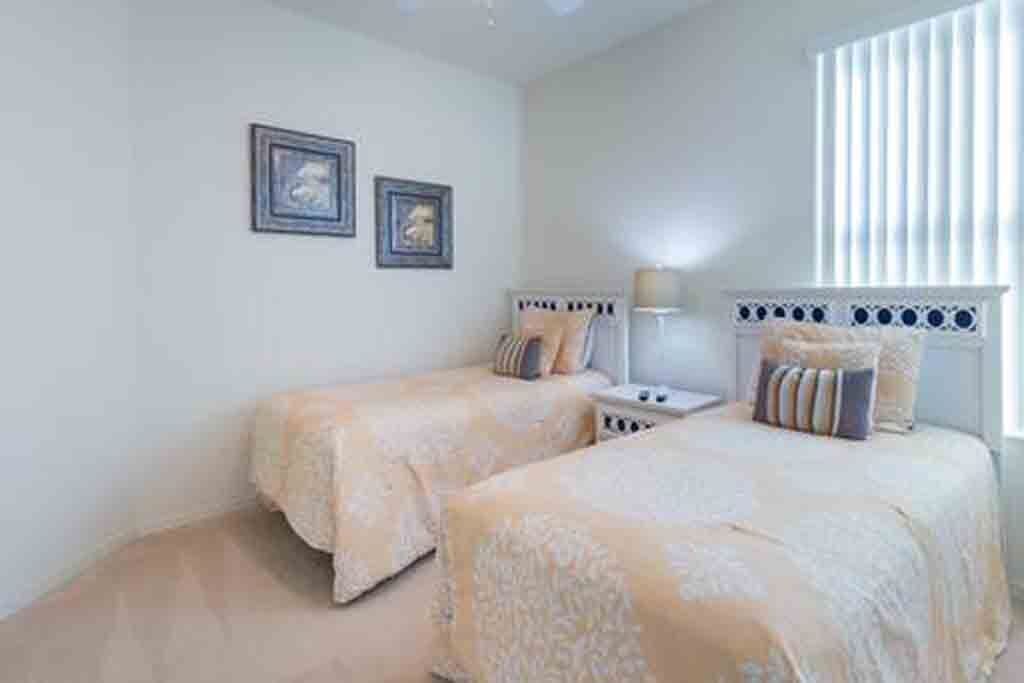 A bedroom with two beds, a nightstand, a lamp, and two framed pictures on the wall.