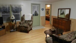 Een woonkamer met houten vloer, een gestreept fauteuil, een bank, een houten dressoir en een televisie op een houten plank.
