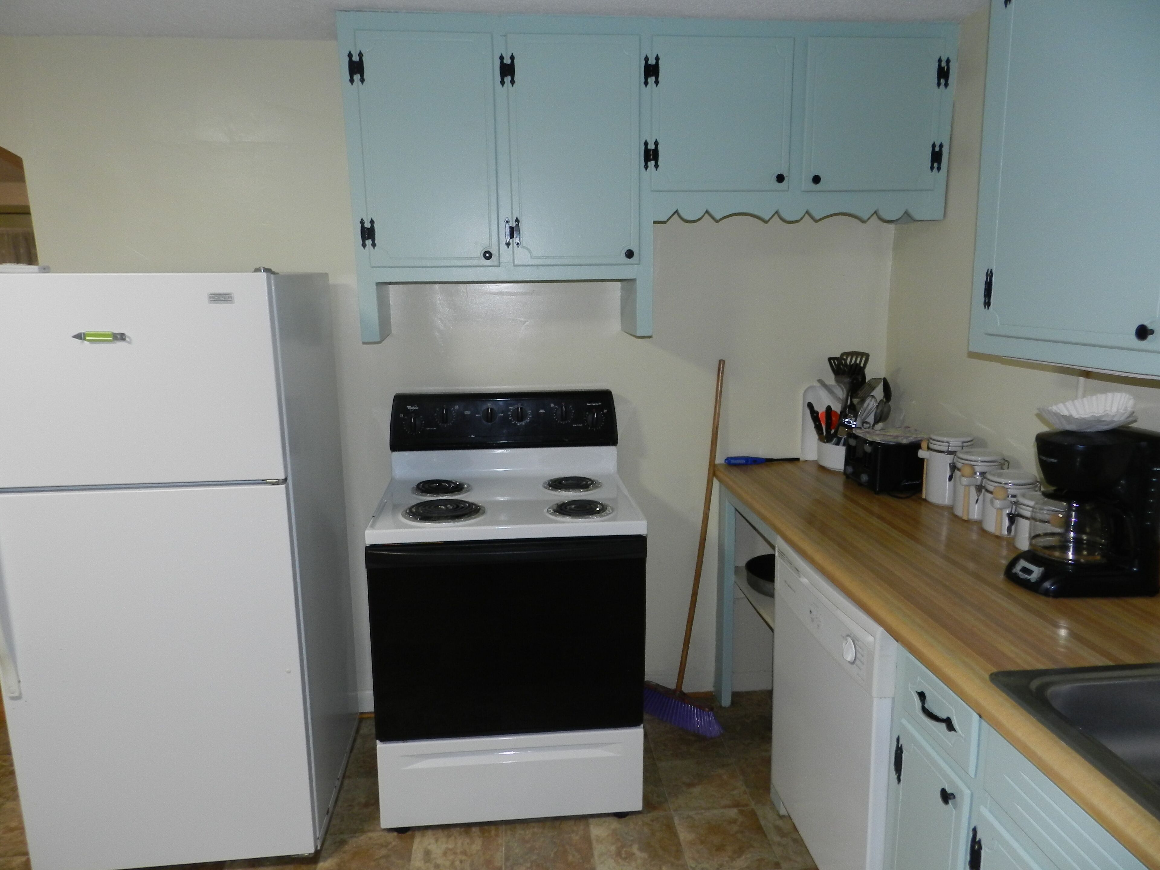 A kitchen with a white refrigerator, a stove, and light blue cabinets.