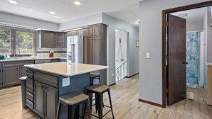 A modern kitchen with a central island, bar stools, and a view to the dining area. - Family Adventure at Lake Wissota Lodge + Studio (Jim Falls)