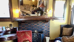 A cozy living room with a red armchair, a brown leather sofa, a fireplace, and a brick wall.