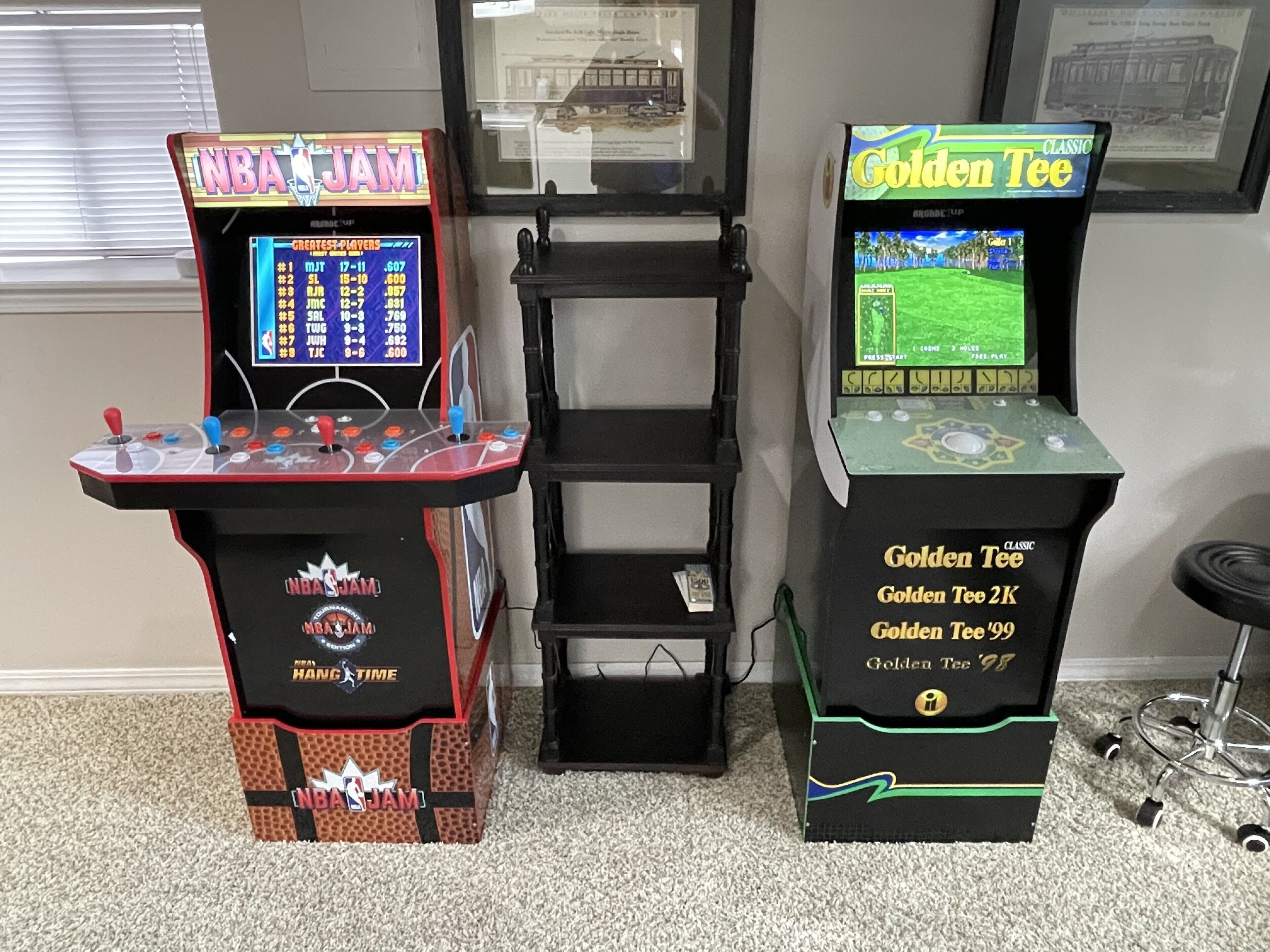 Two arcade machines, one labeled NBA JAM and the other Golden Tee, with a black shelf unit between them.