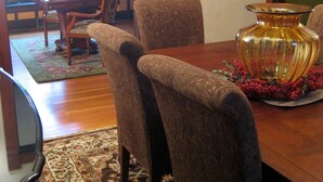 A dining area with a wooden table, patterned chairs, a large decorative vase, and a framed picture on the wall.