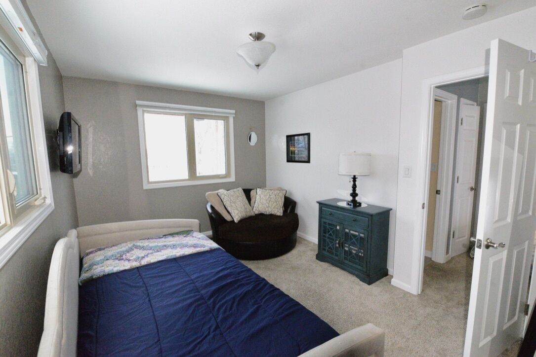Une chambre à coucher avec un lit, une chaise, une table de chevet, une fenêtre et une porte.