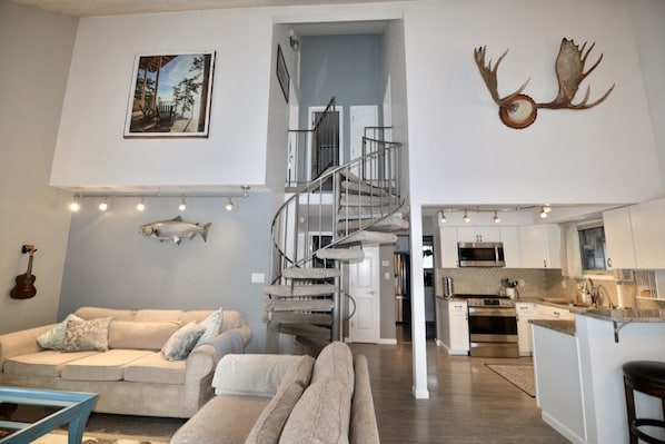 A modern living room with a staircase, a kitchen, and a dining area. - Modern & Unique South Anchorage Home (Anchorage)