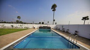 A rectangular swimming pool with a clear blue water surface, surrounded by a white fence, and palm trees in the background. - Neo Farm House with Pool, Beach Volley Ball & 5Beds(A/C) (Batasingaram)