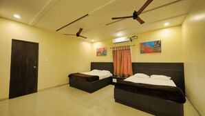 A hotel room with two dark-colored beds, a ceiling fan, an air conditioning unit, and a painting on the wall. - Neo Farm House with Pool, Beach Volley Ball & 5Beds(A/C) (Batasingaram)