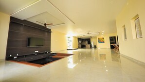 A spacious, modern living area with a flat-screen TV, dark wood entertainment unit, and a polished floor. - Neo Farm House with Pool, Beach Volley Ball & 5Beds(A/C) (Batasingaram)