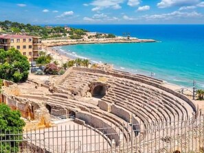 Ein antikes Amphitheater mit gestuften Sitzreihen in Strandnähe und neben Wohngebäuden.