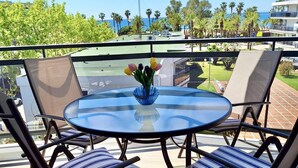 Un balcon avec une table ronde en verre, deux chaises à coussins rayés et un vase rempli de fleurs.