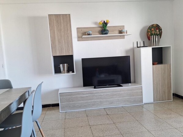 Ein modernes Wohnzimmer mit einem Flachbildfernseher, Holzschränken und einem Essbereich mit Tisch und Stühlen.