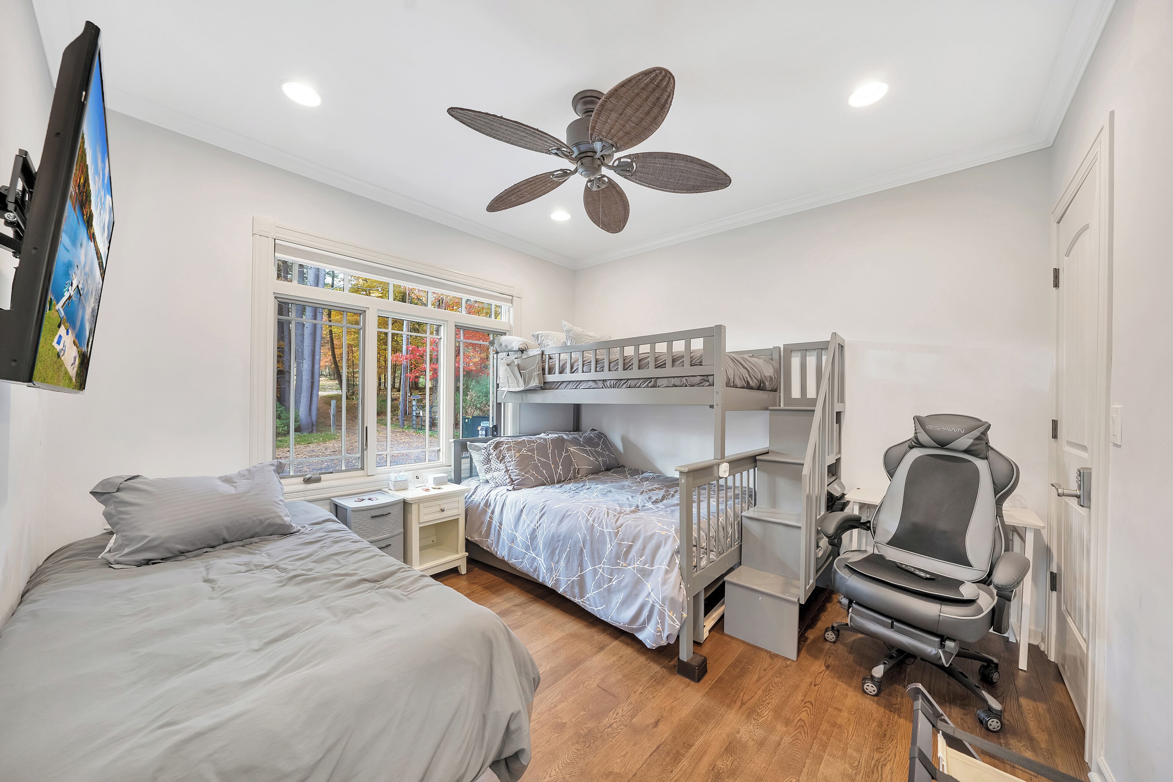 Une chambre avec un lit superposé, un bureau, une chaise, un ventilateur de plafond et une fenêtre donnant sur un beau paysage.