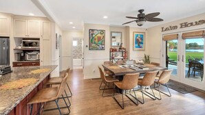 Une cuisine moderne avec un coin repas, comprenant un grand îlot central, des chaises en bois et un ventilateur de plafond.