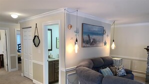 Una sala de estar con un sofá gris, un cuadro de una playa y lámparas colgantes.