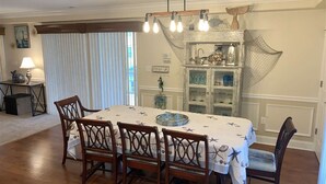 Un comedor con mesa y sillas de madera, una araña y un aparador decorativo con cristalería.