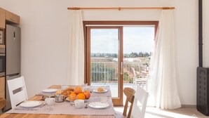 Un'area pranzo con tavolo apparecchiato per la colazione, vista sulla campagna attraverso una porta vetrata e una cucina moderna con forno a incasso.