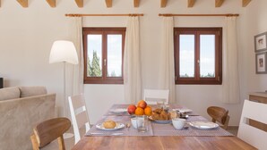 Zona pranzo con tavolo in legno apparecchiata per la colazione, due finestre con tende e un divano sullo sfondo.