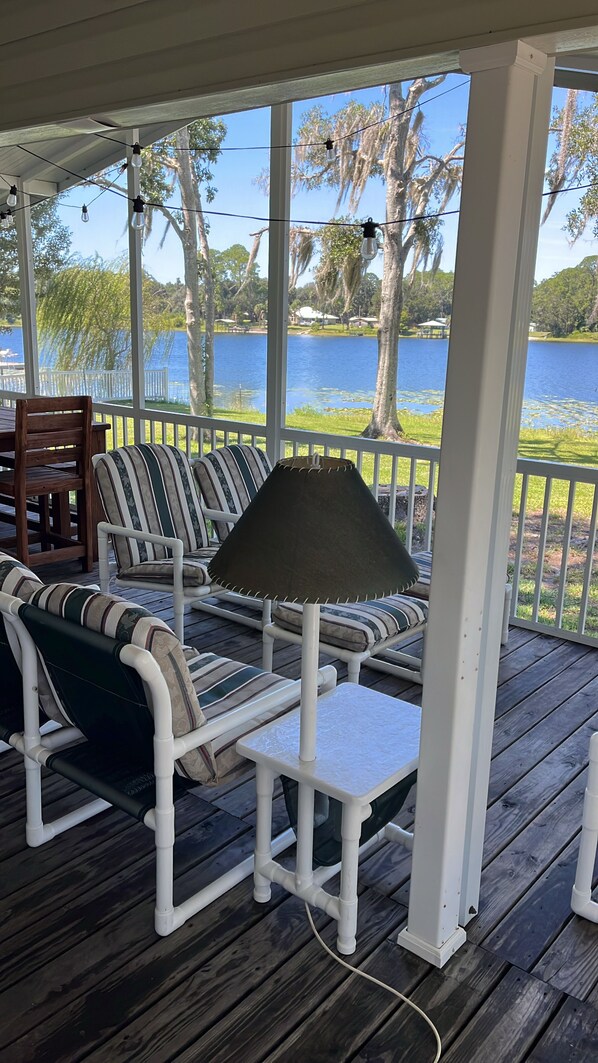 Un espace extérieur abrité, aménagé avec des tables et des chaises dotées de coussins à rayures, et offrant une vue sur un lac.