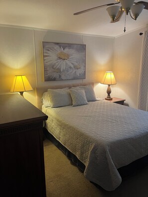 Une chambre à coucher avec un lit, deux lampes de chevet, un ventilateur de plafond et un tableau représentant des fleurs accroché au mur.